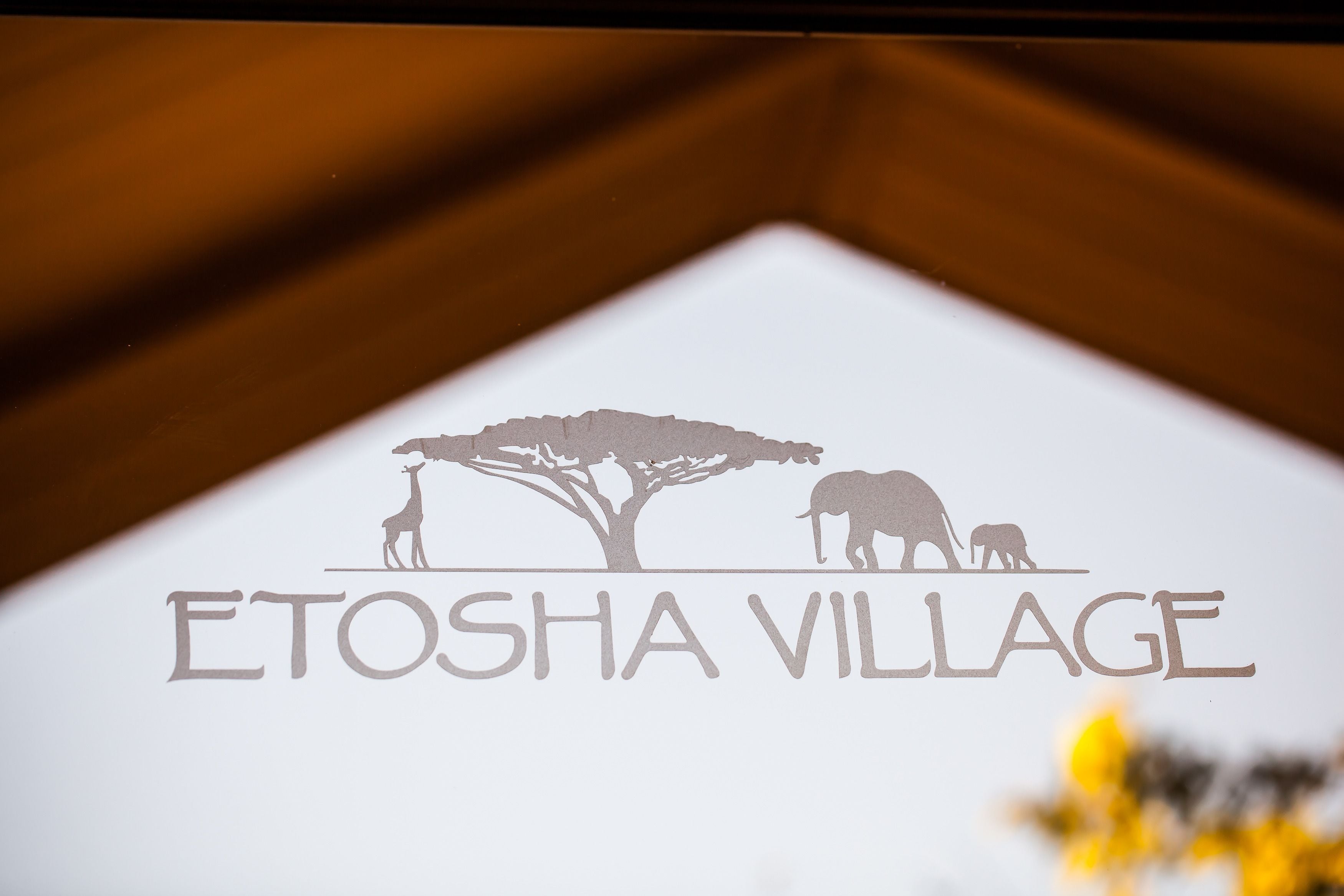 Un logo représentant une girafe, un éléphant et un arbre, ainsi que le texte « ETOSHA VILLAGE ».