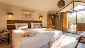A double bed with a zebra-patterned pillow, a bedside table with a lamp, and a large window with curtains. - Etosha Village (Okaukuejo)