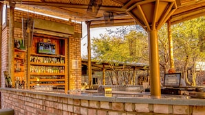 An outdoor bar area with brick walls, shelves stocked with bottles, and a television screen. - Etosha Village (Okaukuejo)
