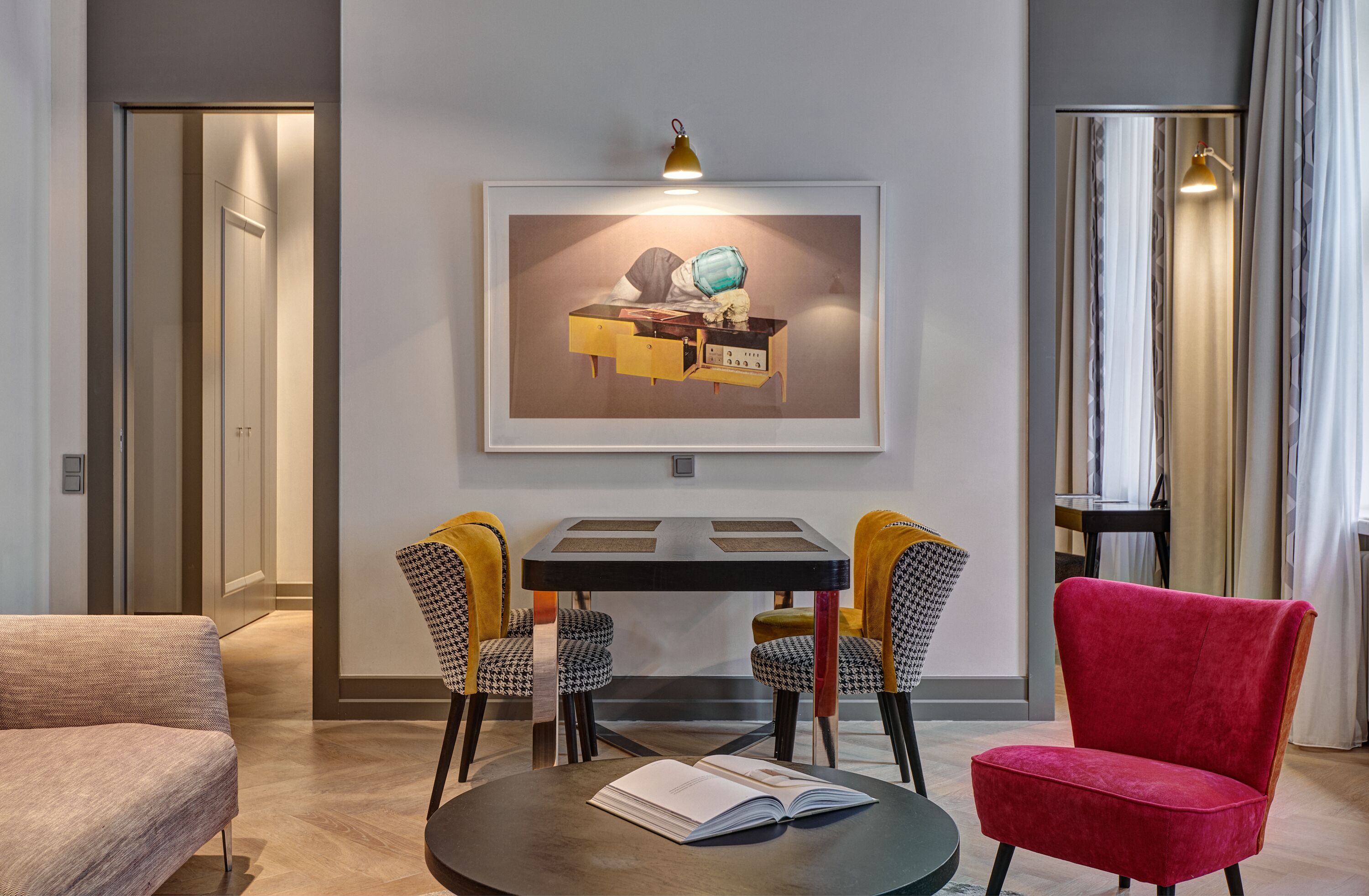 A modern living room with a dining table, two chairs, a red armchair, and a framed artwork on the wall.