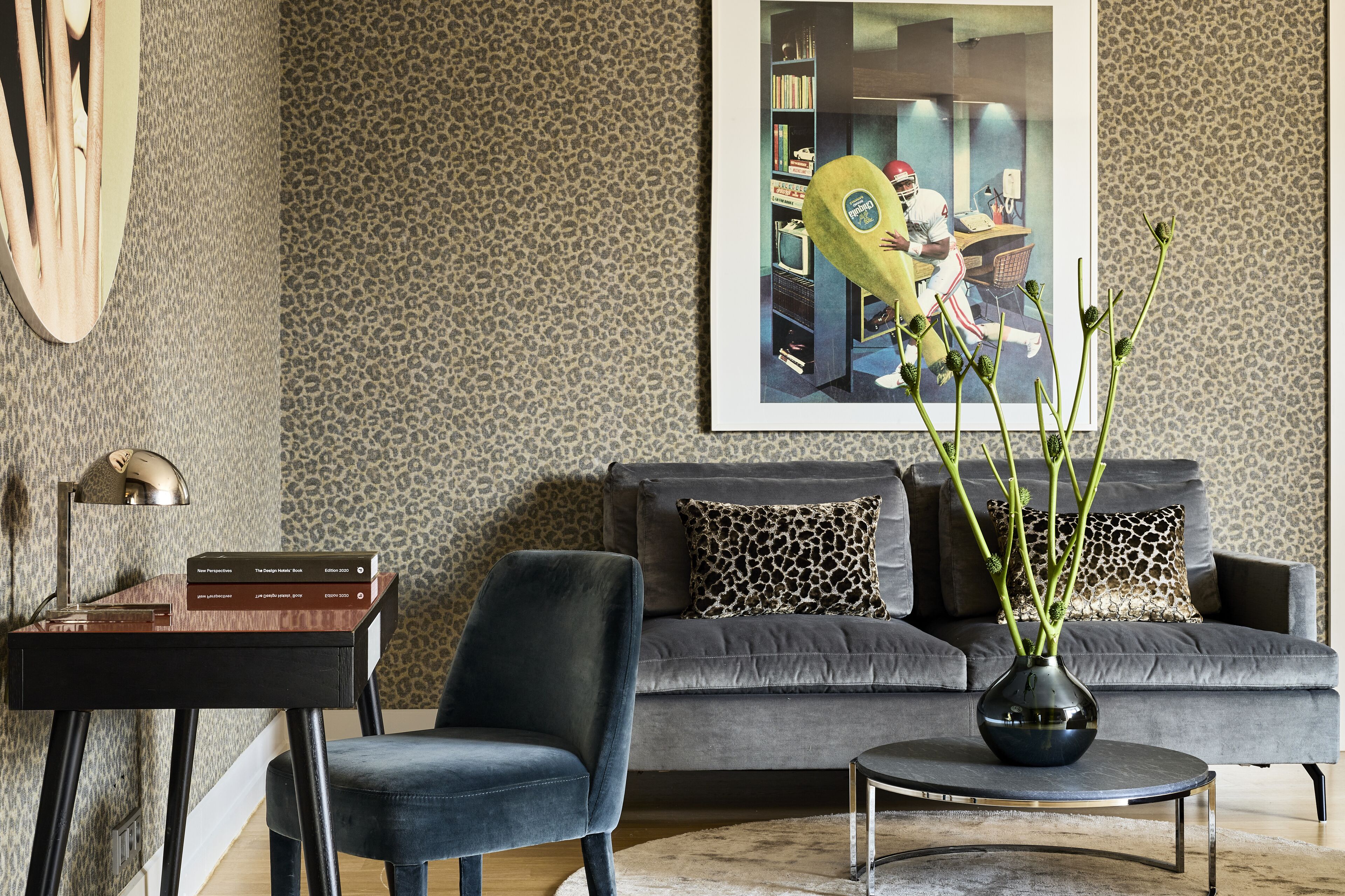 Un salon moderne avec un canapé gris, un fauteuil noir, une petite table sur laquelle est posé un vase, et une bibliothèque.