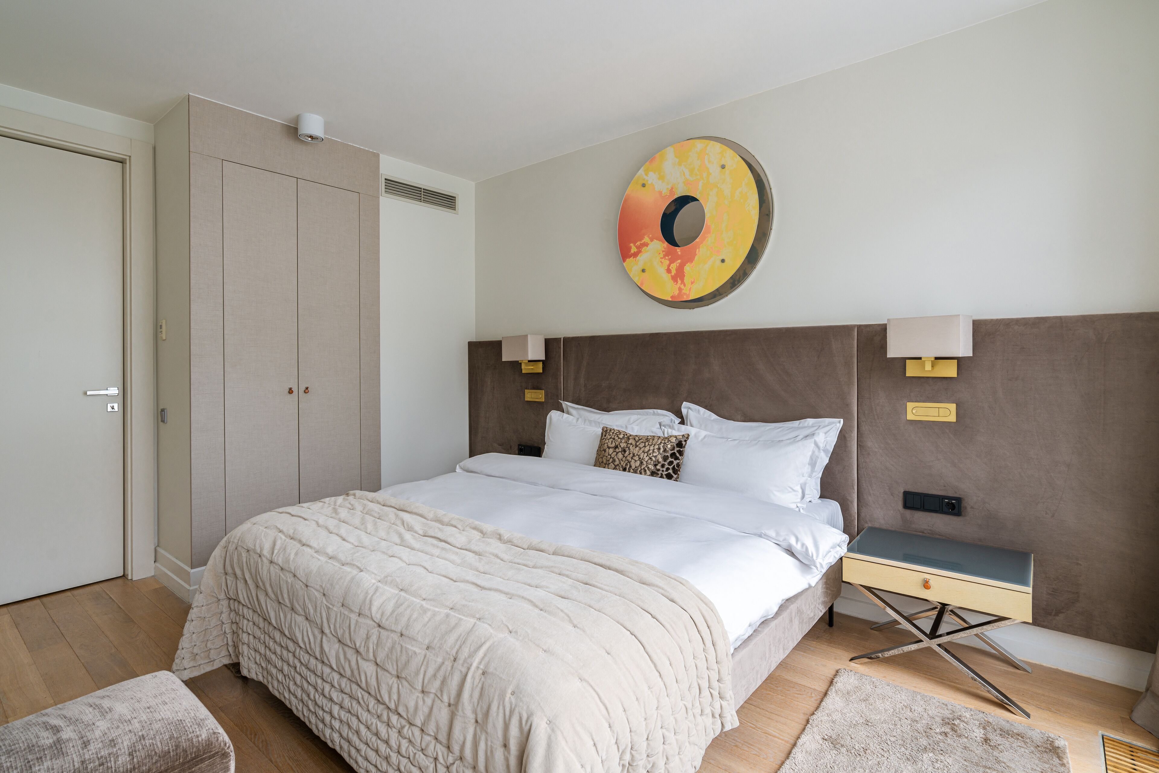 Une chambre à coucher comprenant un lit, des tables de chevet, une armoire et une œuvre d’art accrochée au mur.