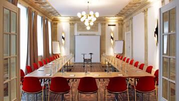 Un salón de conferencias con una larga mesa, sillas rojas y una pantalla de proyector al frente.