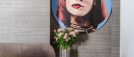 A modern living room with a grey sofa, a decorative vase with flowers, and a wall-mounted artwork.