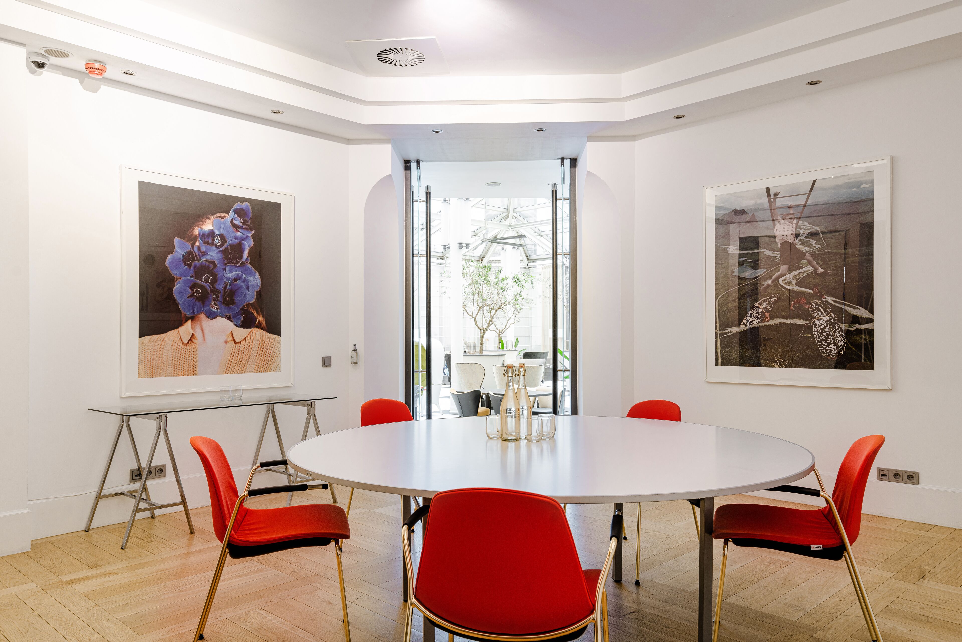 A conference room with a round table, red chairs, and two framed artworks on the walls.