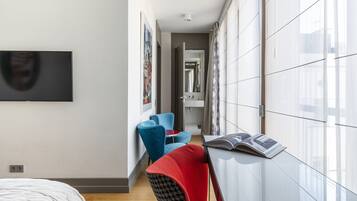 Una habitación de hotel moderna con una cama, un televisor, una silla roja, una silla azul y una revista sobre una mesa.