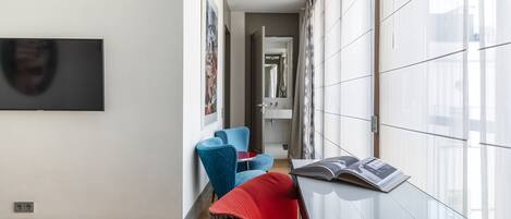 Una habitación de hotel moderna con una cama, un televisor, una silla roja, una silla azul y una revista sobre una mesa.