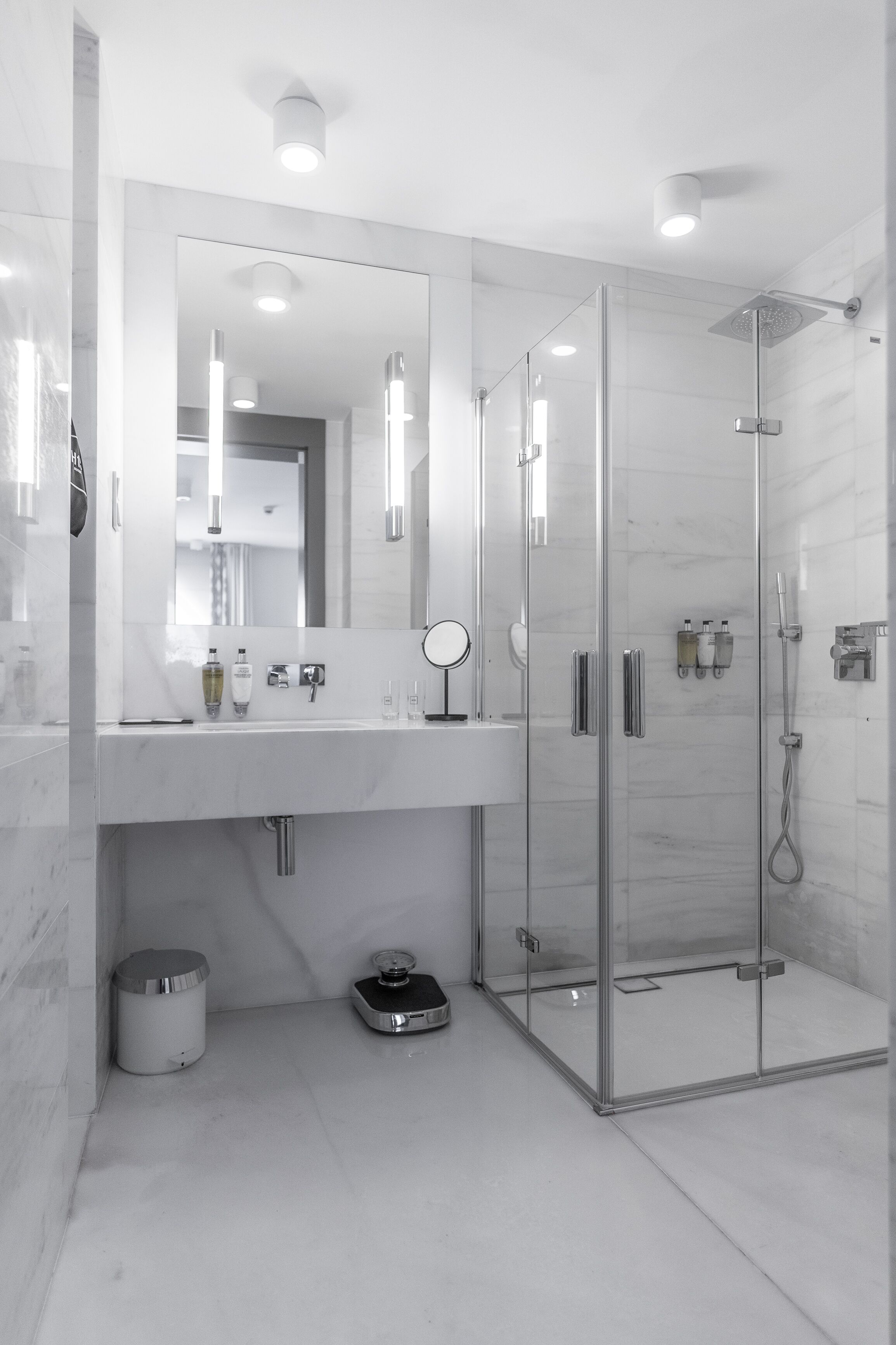 A modern bathroom with a glass-enclosed shower, a large mirror, and a white marble countertop.