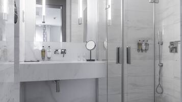A modern bathroom with a glass-enclosed shower, a large mirror, and a white marble countertop.