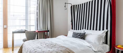 Quarto de hotel bem arrumado, com uma cama grande, uma escrivaninha e uma cadeira.