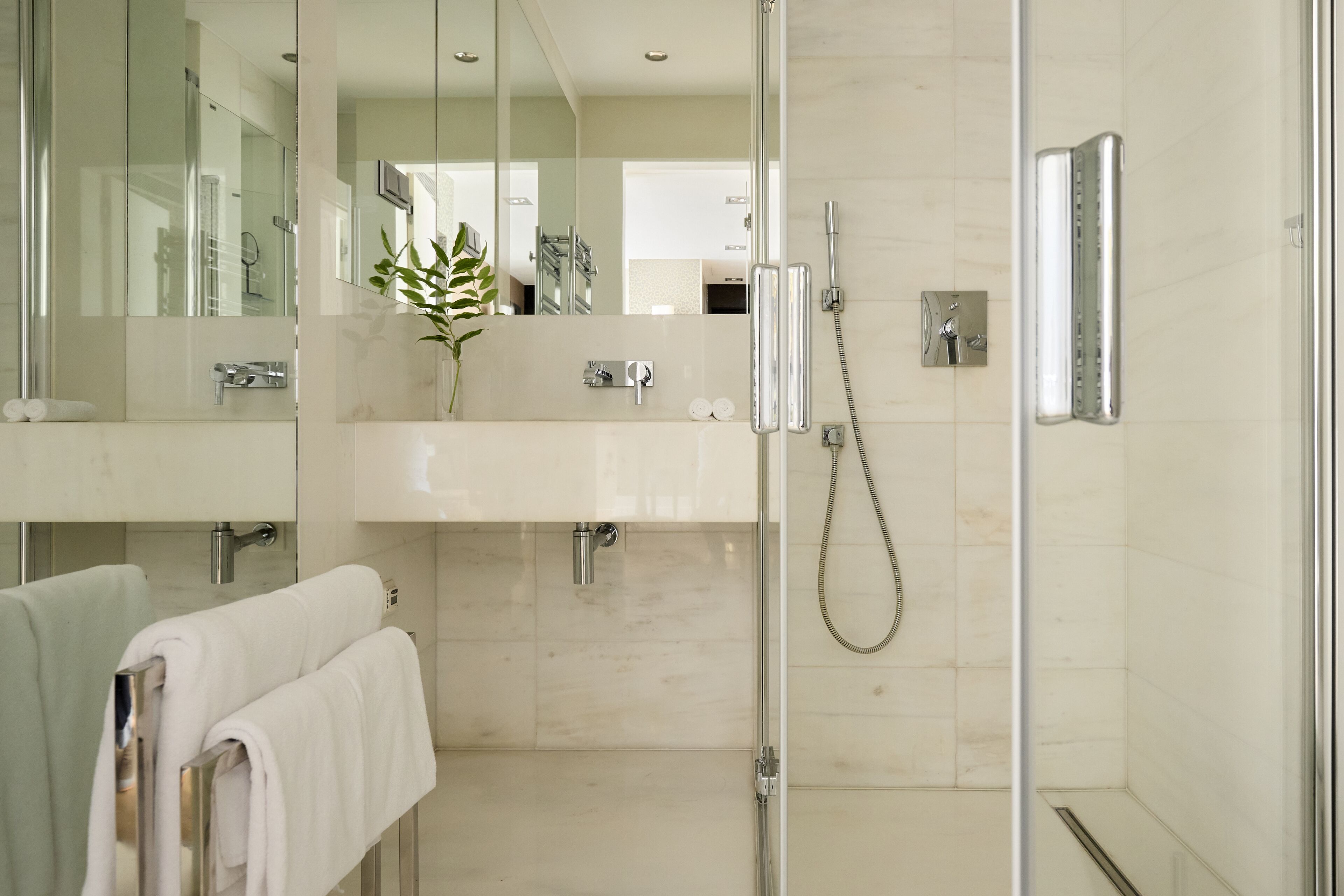 A modern bathroom with a glass shower enclosure, a sink with a mirror, and two towels hanging on a rack.