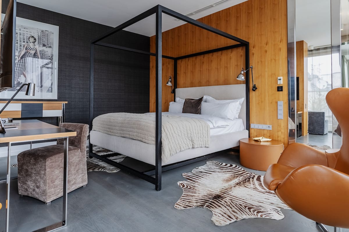 A modern bedroom with a four-poster bed, a desk, and a leather chair.