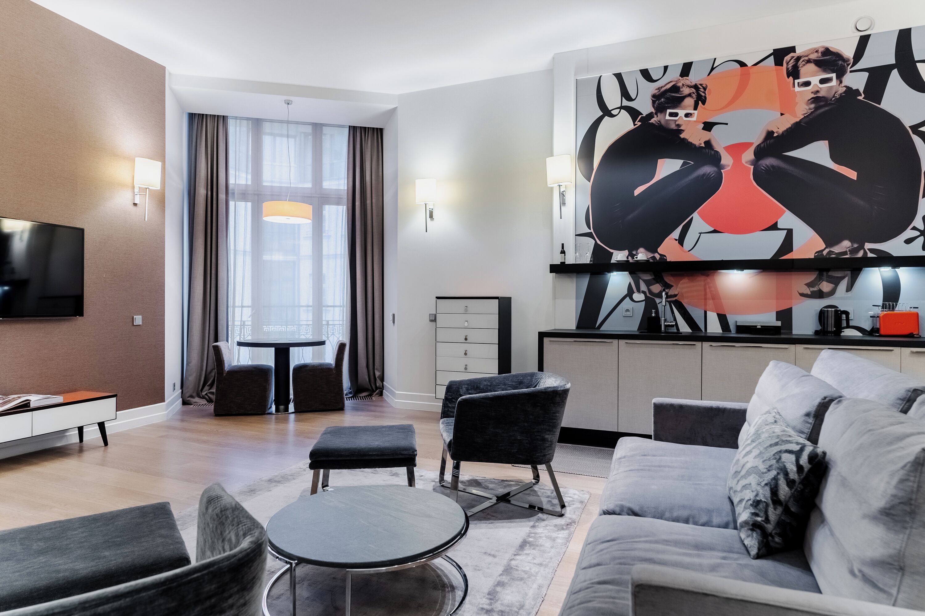 A modern living room with a flat-screen TV, a dining area with a table and chairs, and a kitchen area with a microwave and coffee maker.