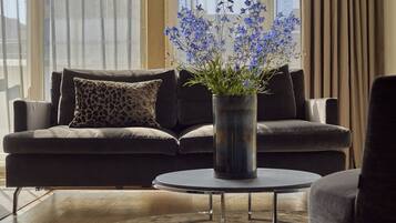 Una sala de estar moderna con un sofá gris oscuro, un cojín estampado de leopardo, una mesa de centro redonda y un jarrón con flores azules.