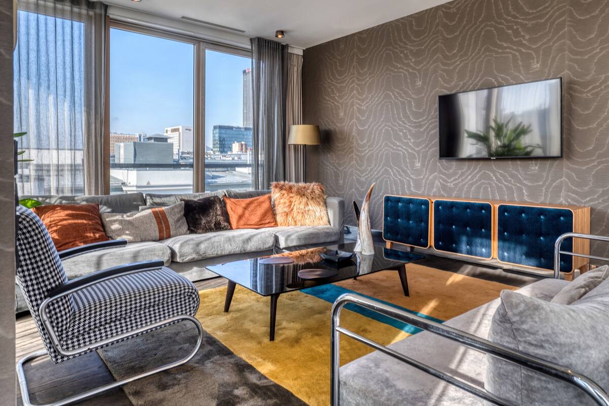 A modern living room with a sofa, armchairs, a coffee table, and a TV mounted on the wall.