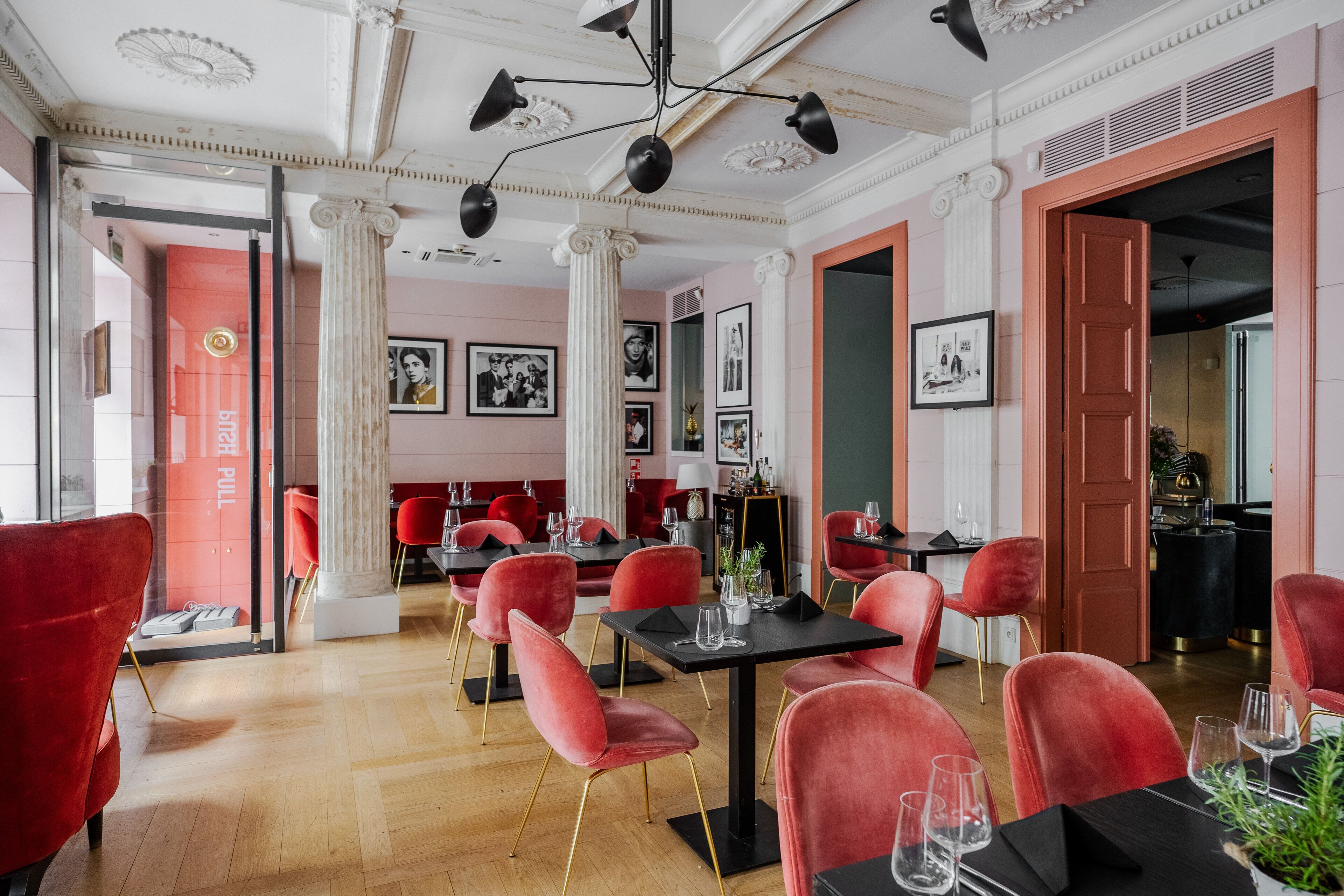 Un restaurante con sillas rojas y mesas negras, columnas y cuadros en las paredes.