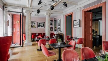 Un restaurante con sillas rojas y mesas negras, columnas y cuadros en las paredes.