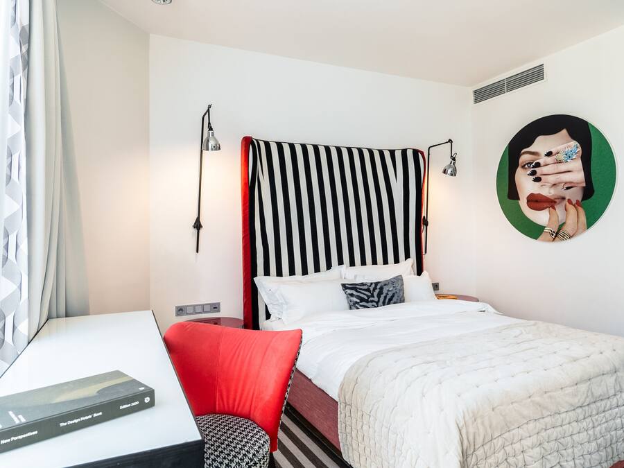 A hotel room with a bed, a desk, and a chair. There is a book on the desk and a painting on the wall.