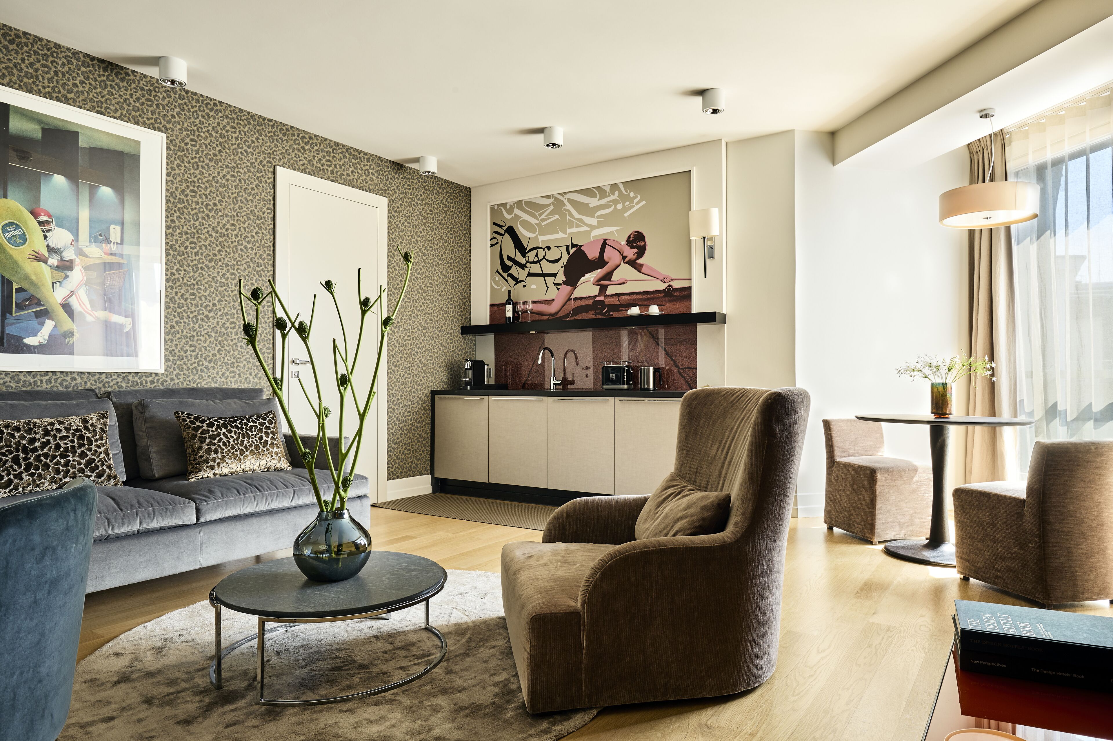 Un salon moderne comprenant un canapé, des fauteuils, une table basse et un coin cuisine avec un plan de travail et des placards.