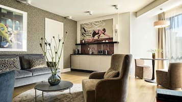 Un salon moderne comprenant un canapé, des fauteuils, une table basse et un coin cuisine avec un plan de travail et des placards.