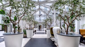 A modern hotel lobby with a glass ceiling, potted trees, and contemporary seating.
