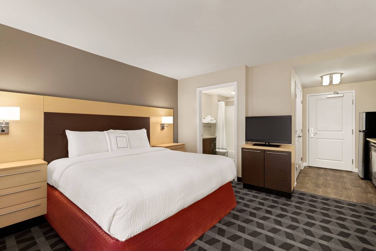 Ein Hotelzimmer mit einem großen Bett, einem Fernseher, einem Schreibtisch und einem Kleiderschrank.