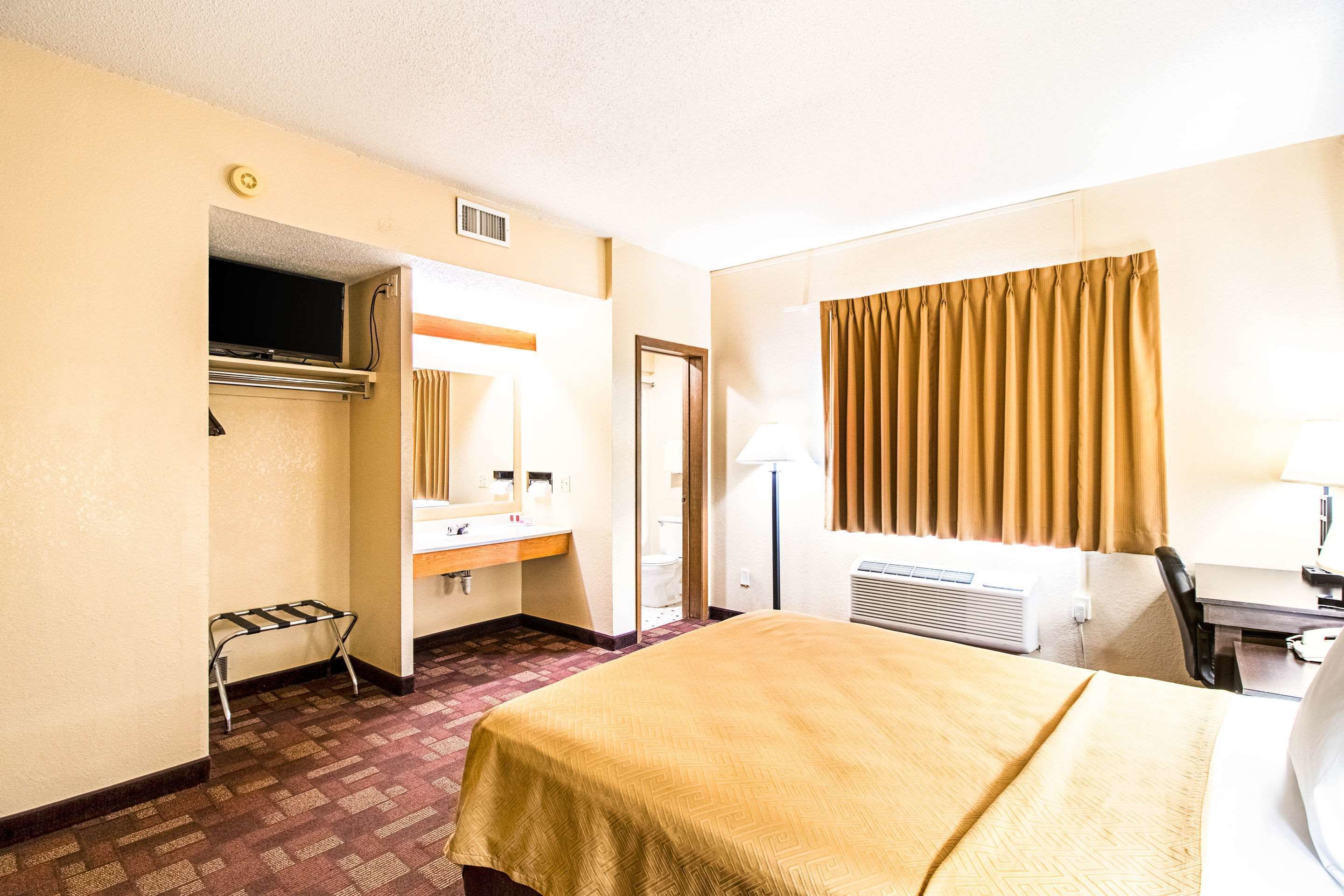 A hotel room with a bed, a desk, a chair, a bathroom, and a television.