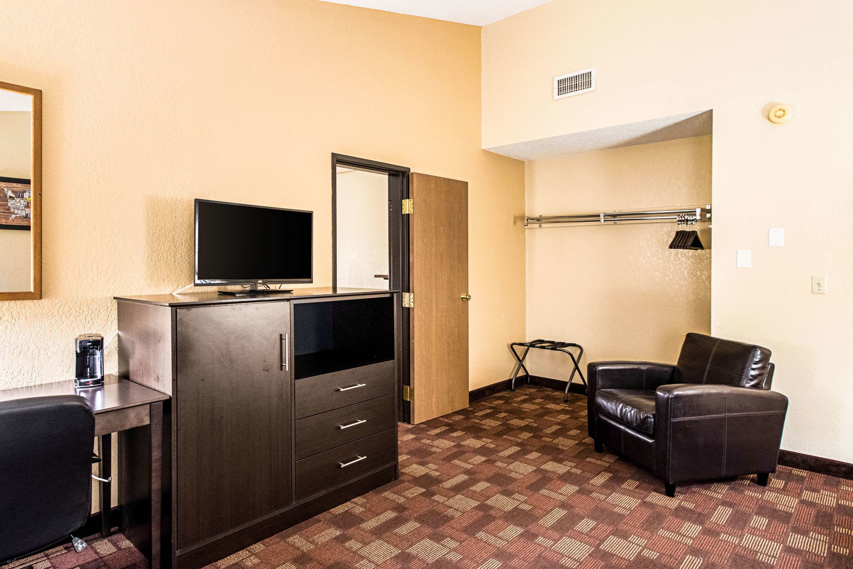 A hotel room with a dark wooden cabinet, a flat-screen TV, a leather armchair, and a patterned carpet.