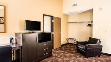 A hotel room with a dark wooden cabinet, a flat-screen TV, a leather armchair, and a patterned carpet.