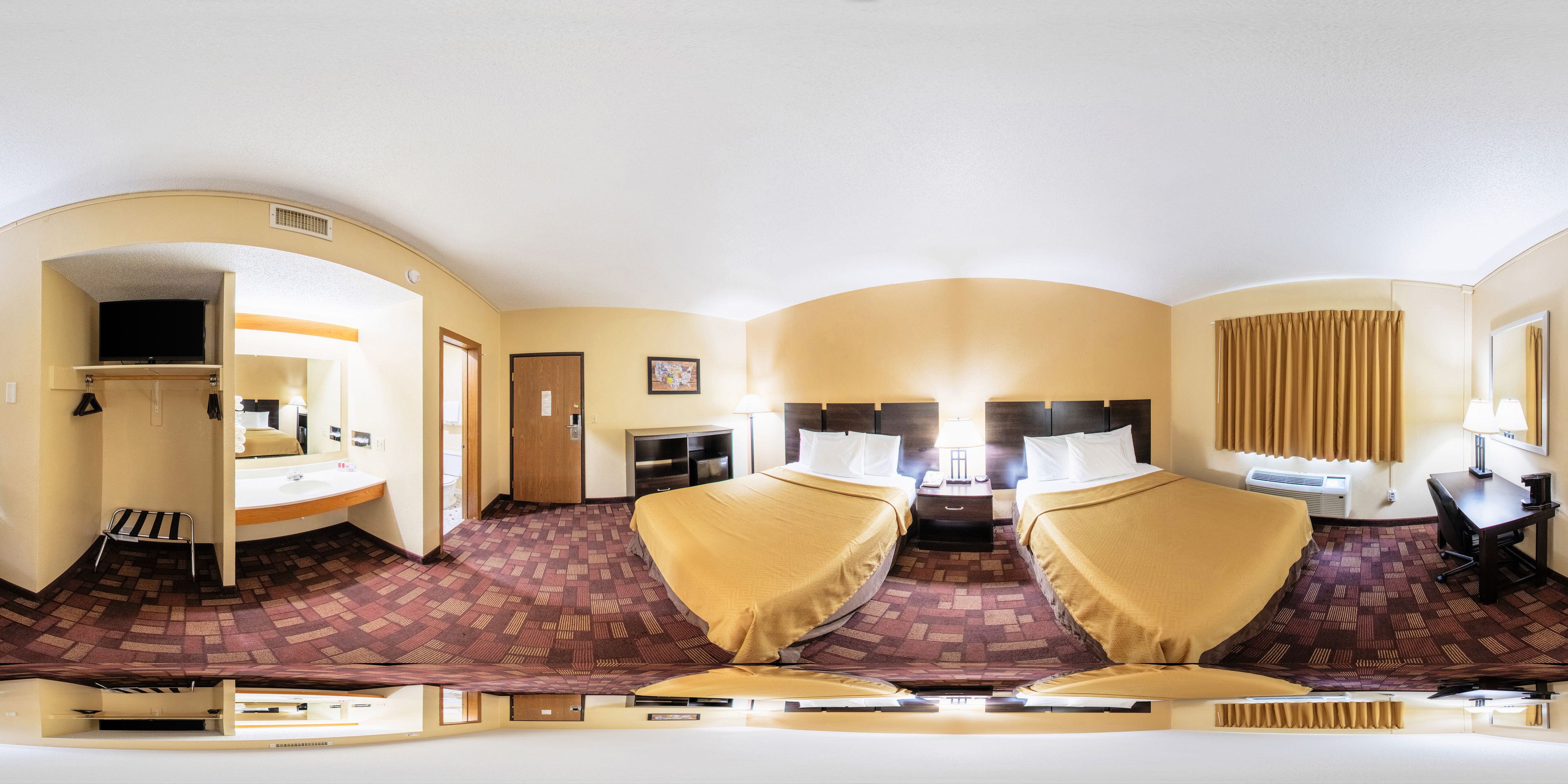 Een hotelkamer met een spiegelkast, een bureau, een bed met hoofdeinde, en een badkamer met wastafel en spiegel.