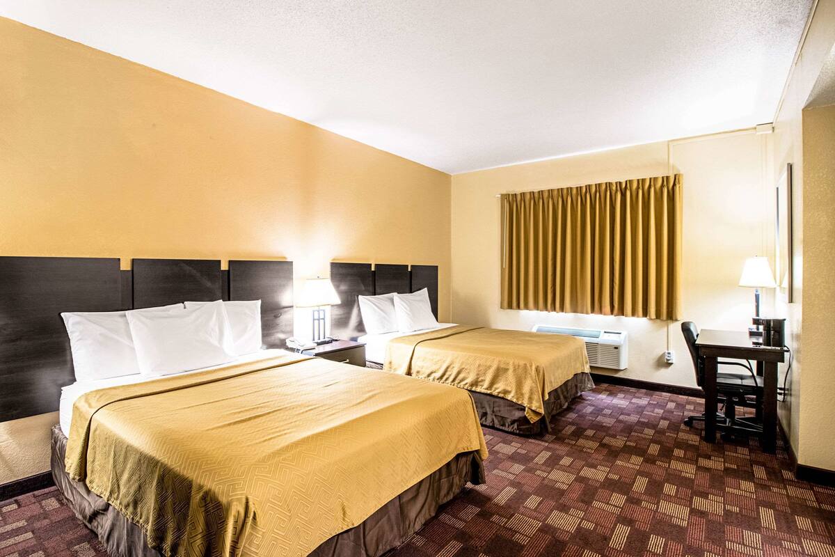 A hotel room with two beds, a desk, and a chair.