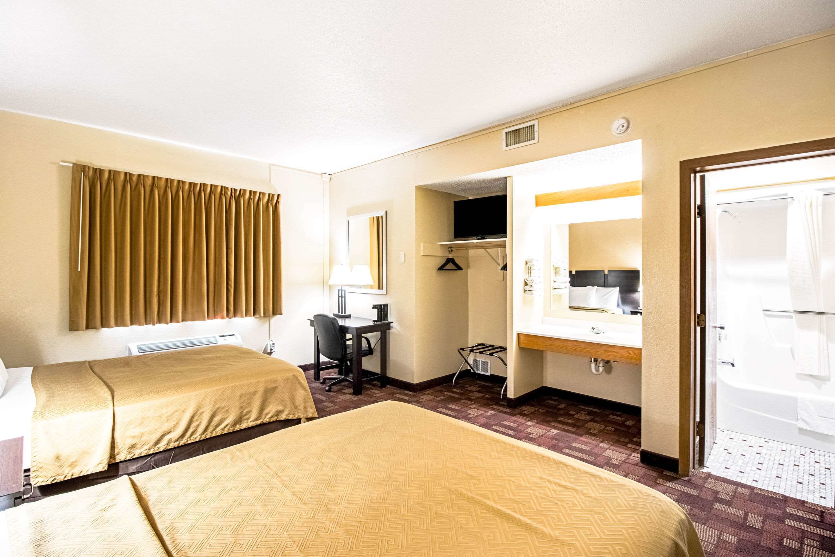 A hotel room with two beds, a desk, a TV, a bathroom, and a shower.