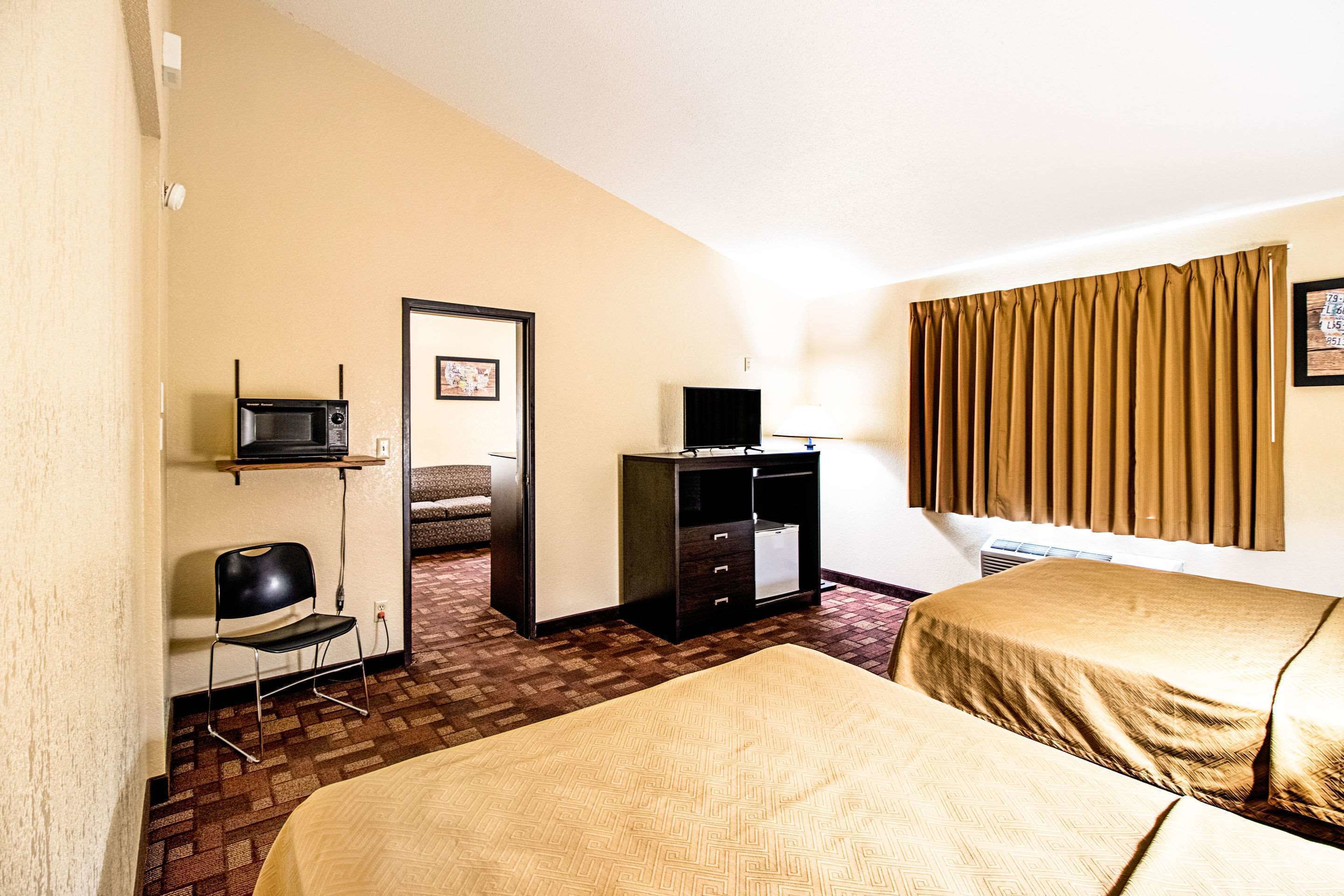 Una habitación de hotel con una cama, un escritorio con una silla, un televisor y una ventana con cortinas.