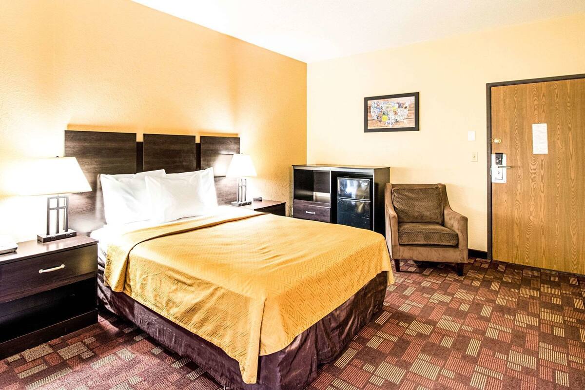 A hotel room with a bed, nightstands, a chair, a television, and a door.