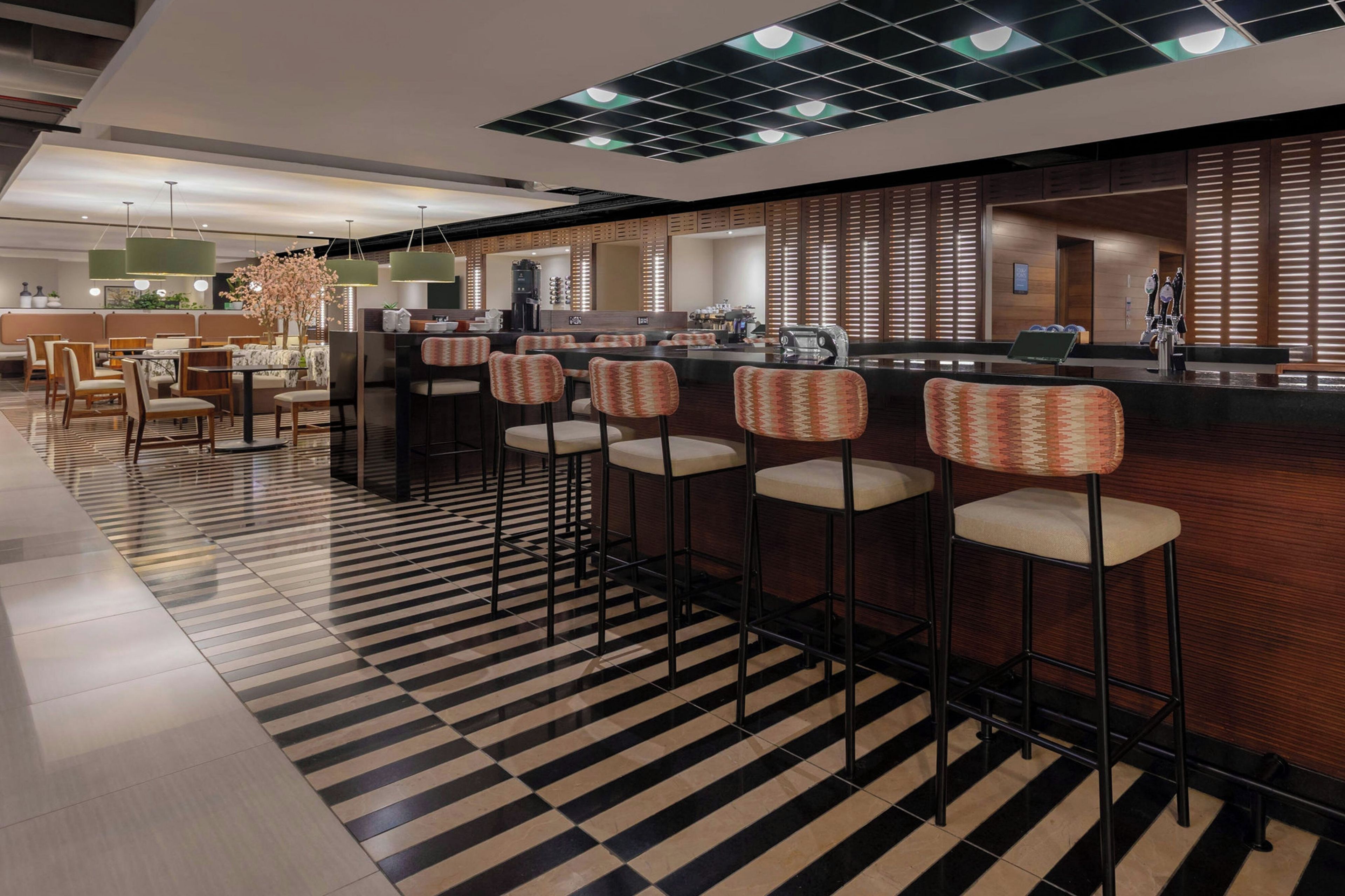 Un área de bar moderna con taburetes altos, piso a cuadros y una barra.