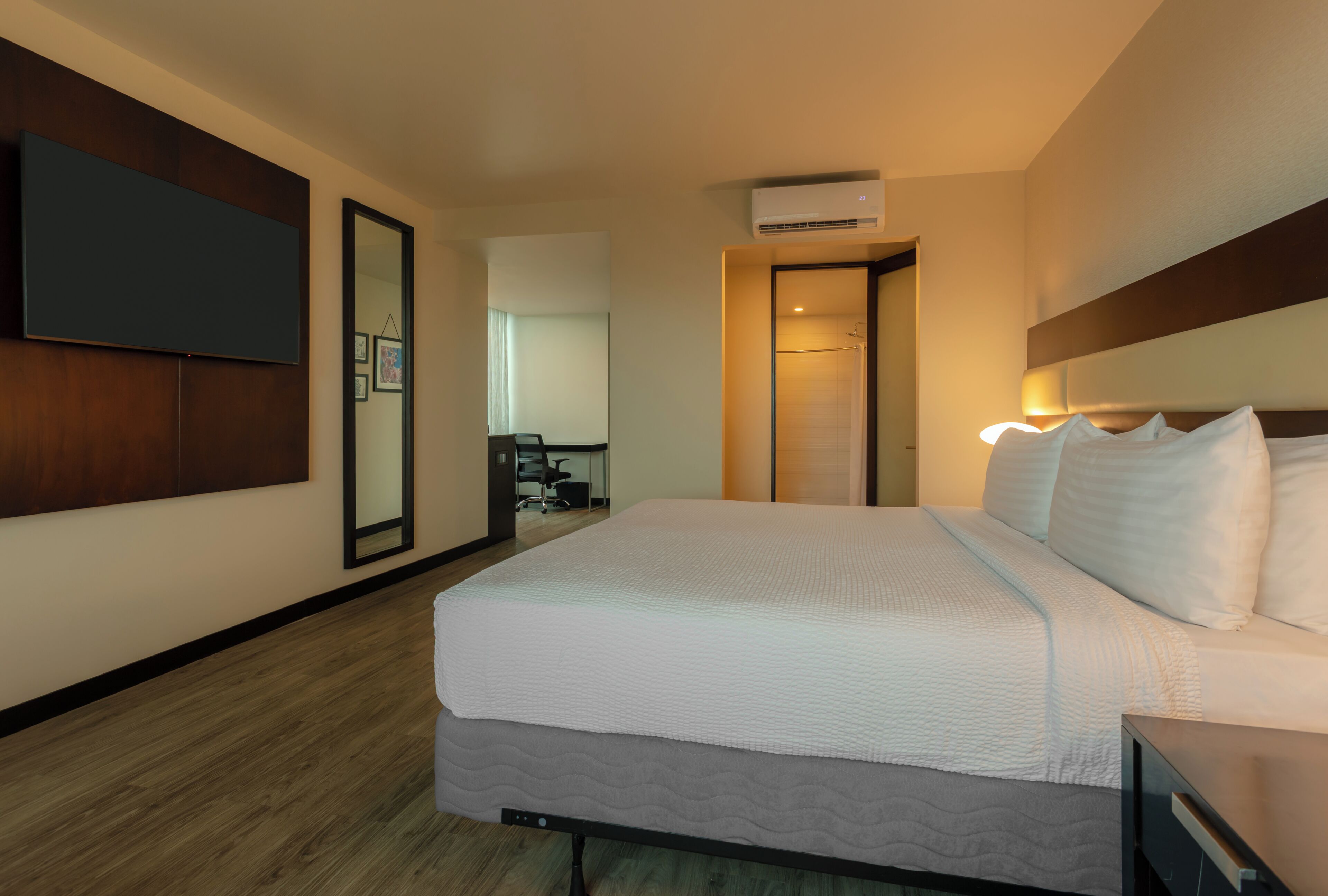 Hotelkamer met een groot bed, een flatscreen televisie aan de wand, een airconditioning en een houten vloer.