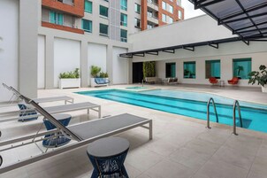 Un área de piscina moderna al aire libre con sillones de descanso, una mesita y plantas en macetas.