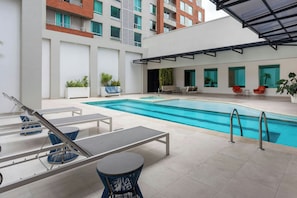 A modern outdoor pool area with lounge chairs, a small table, and potted plants.