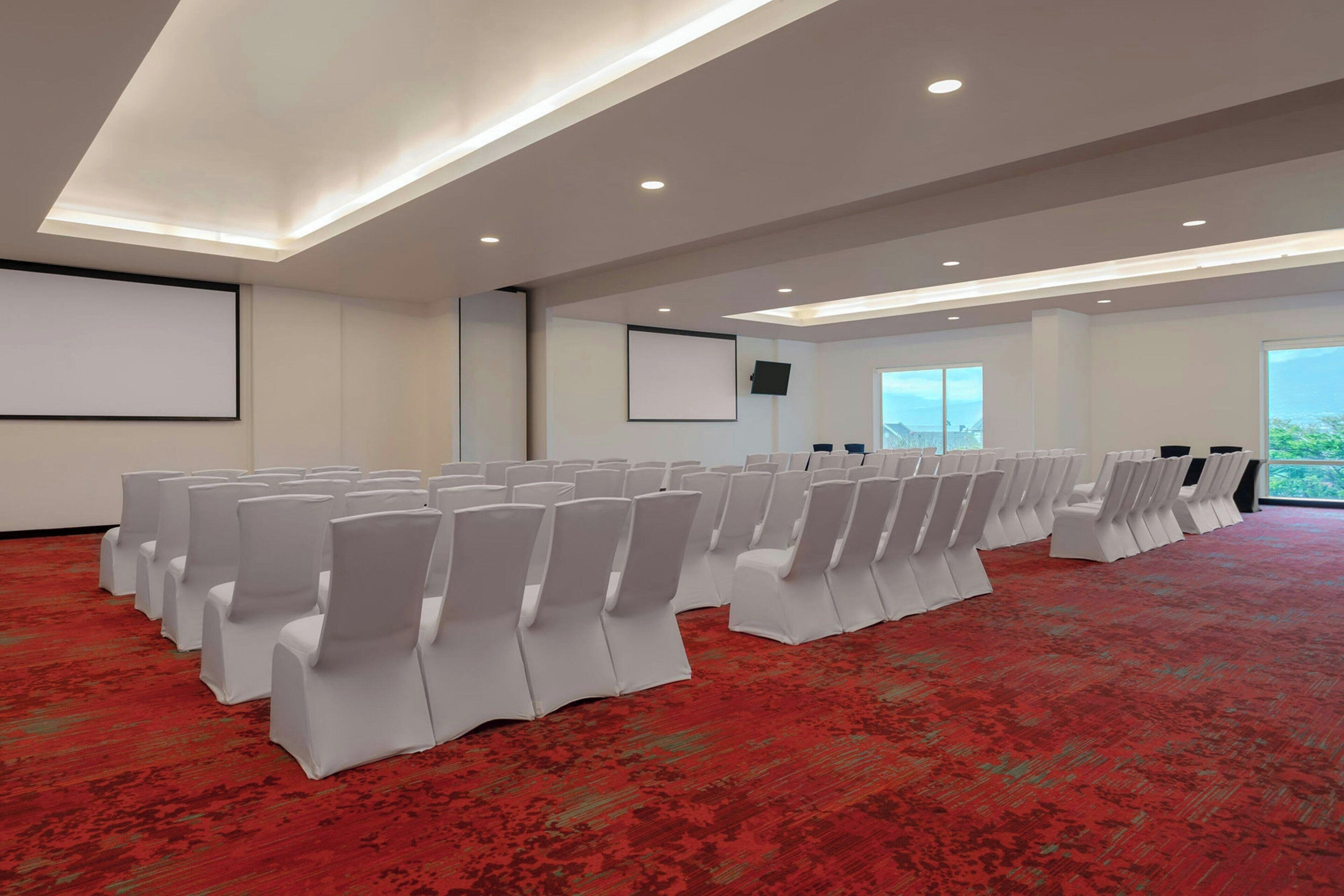 Ein Konferenzraum mit Reihen weißer Stühle, einer großen Leinwand und einem Projektor.