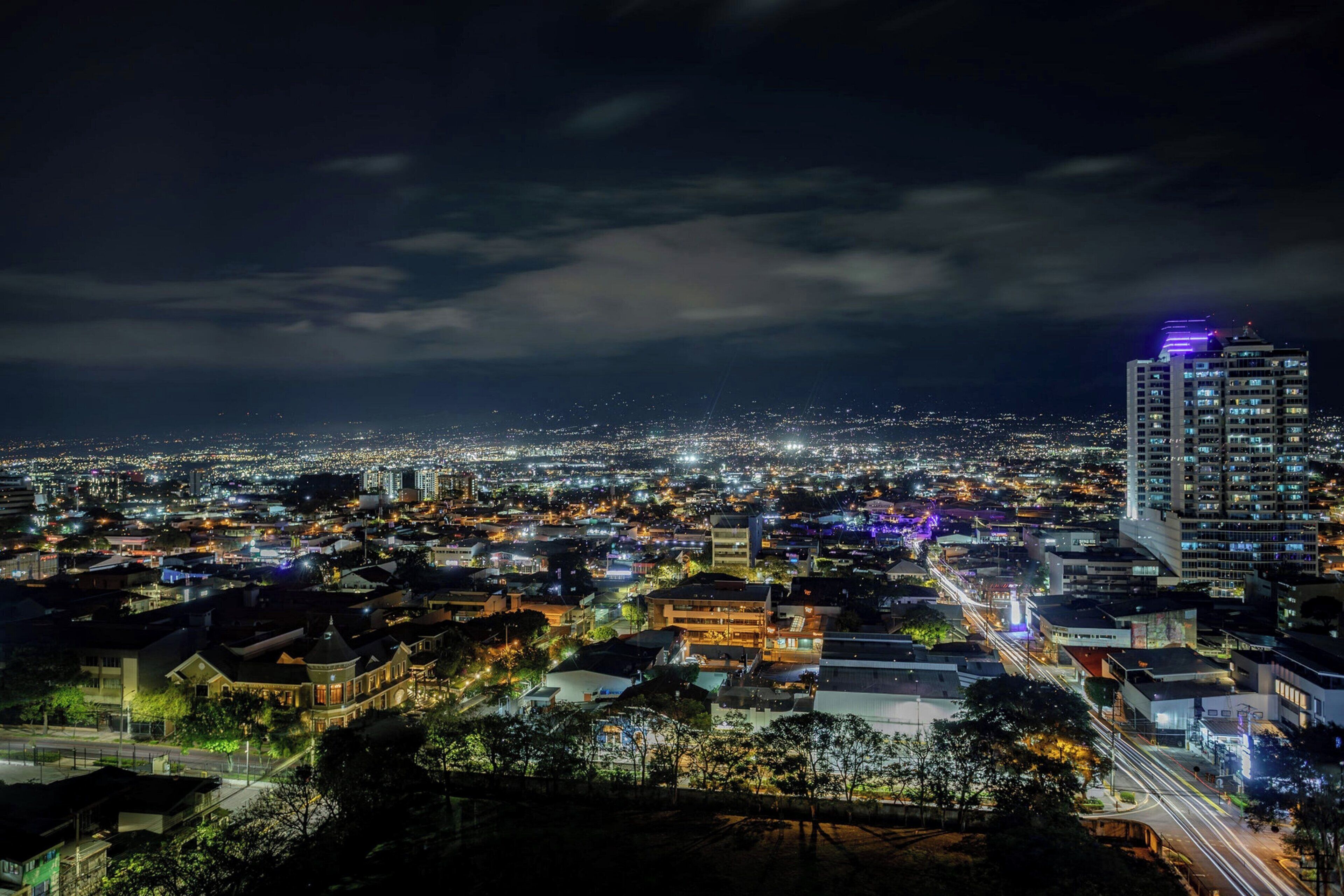 A nighttime cityscape with a prominent high-rise building and a dense urban area.