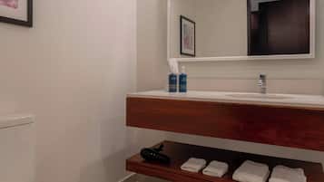Een moderne badkamer met toilet, een houten wastafelmeubel met spiegel en een plank met handdoeken.