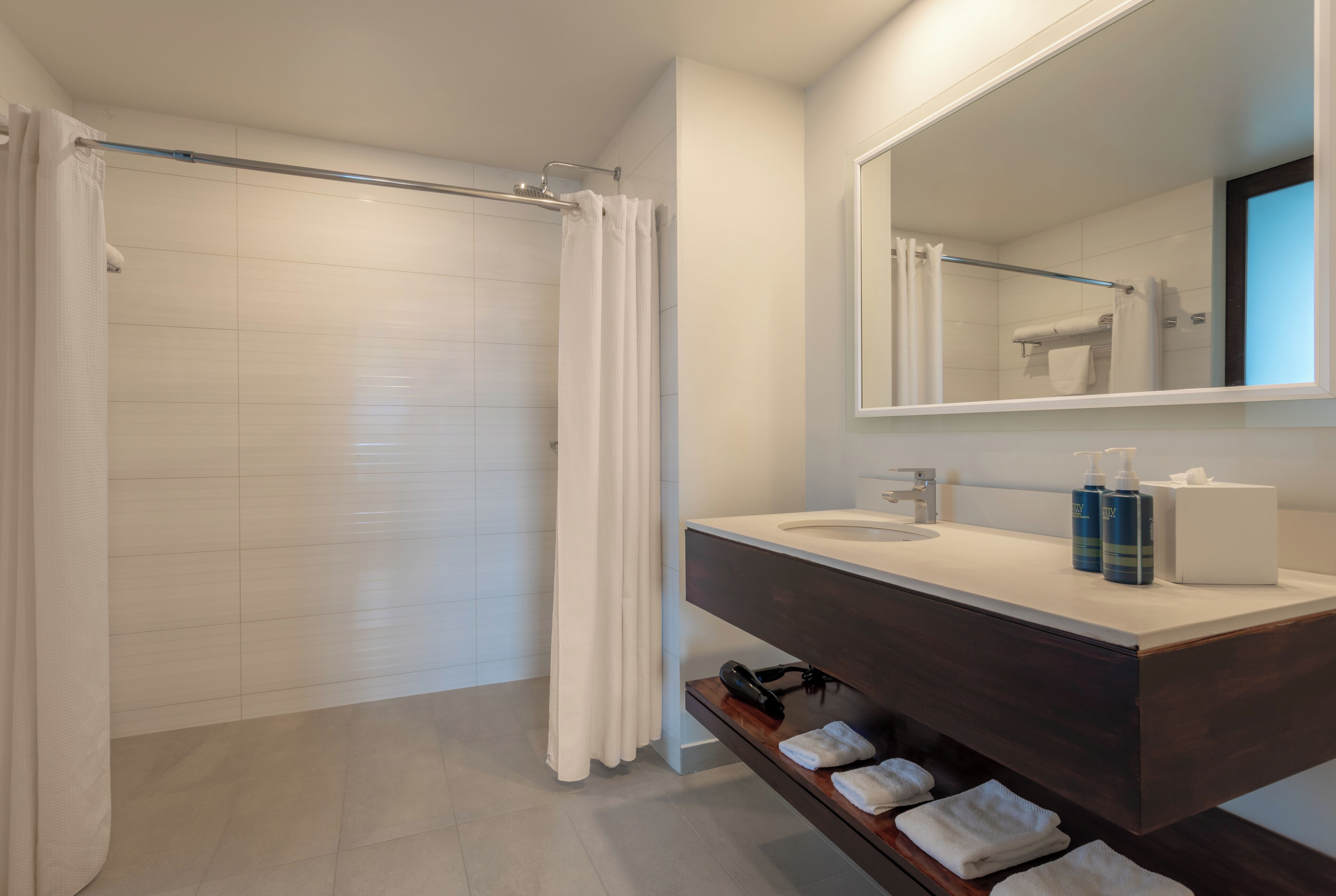 Une salle de bain moderne équipée d’une douche, d’un meuble-lavabo avec miroir et d’un porte-serviettes.