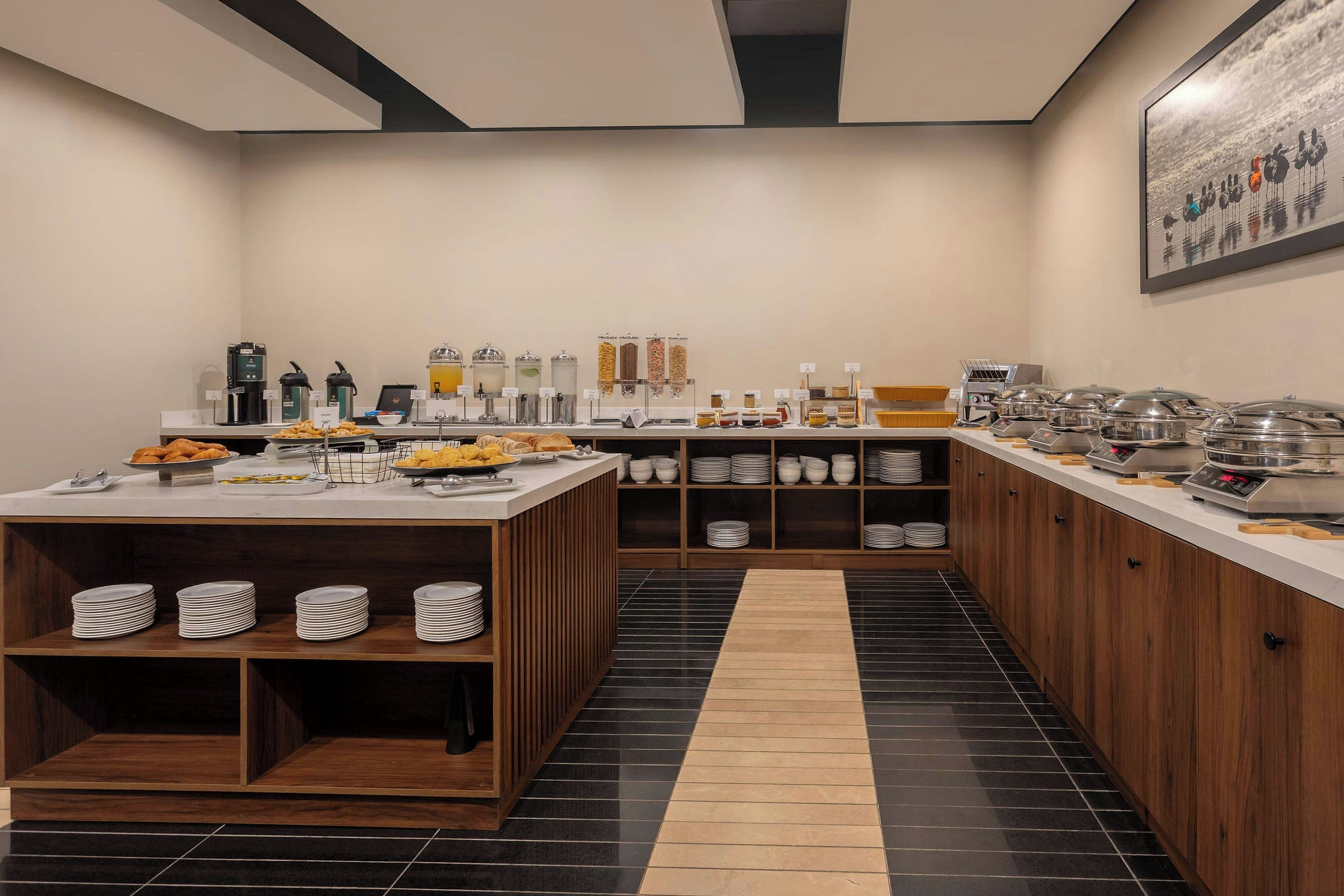 Eine moderne Frühstücksbar mit vielfältigen Speisen, Kaffeeautomaten und einem Buffetbereich mit gestapelten Tellern und Schüsseln.
