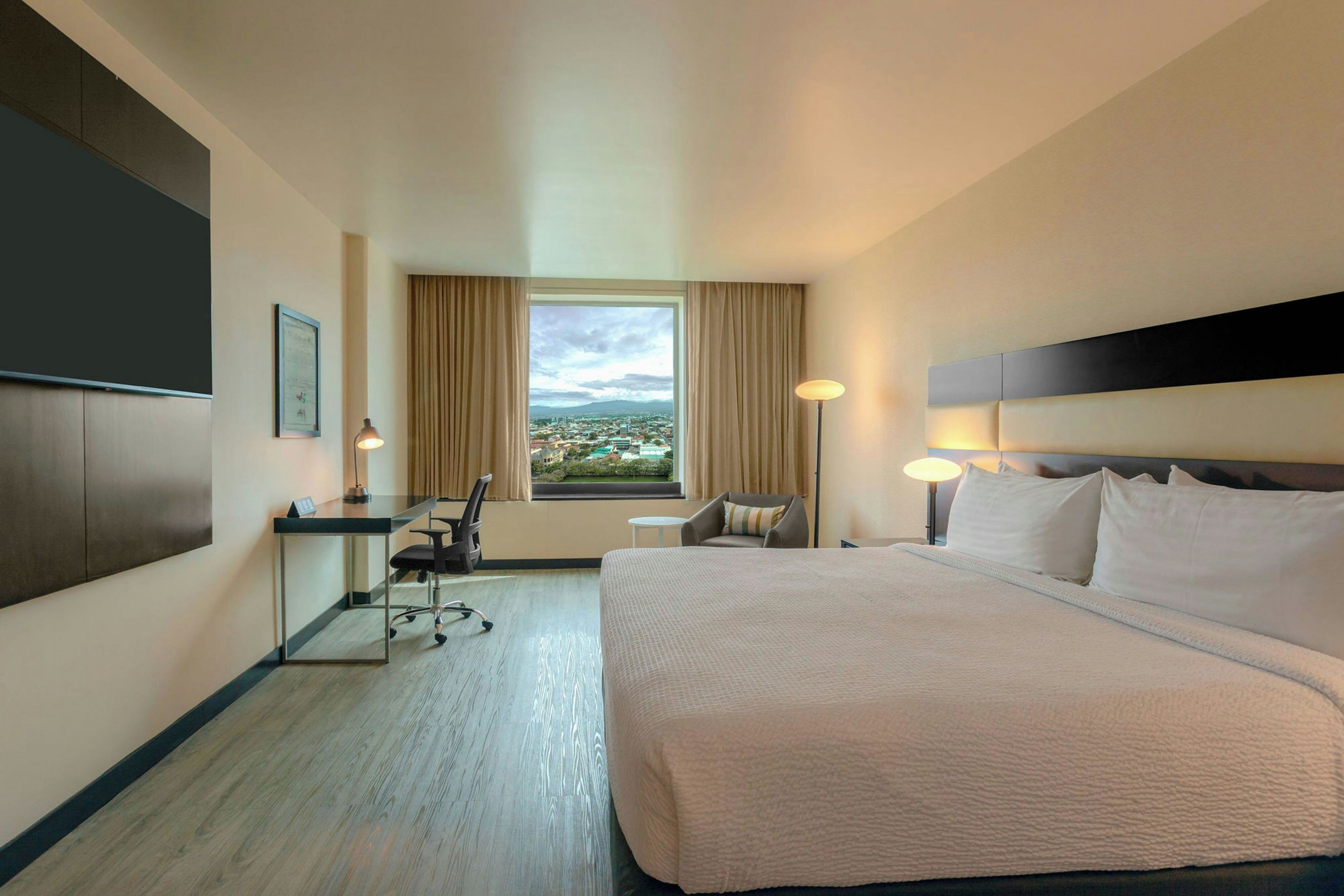Een hotelkamer met een groot bed, een bureau, een stoel, een televisie en een raam met uitzicht over de stad.