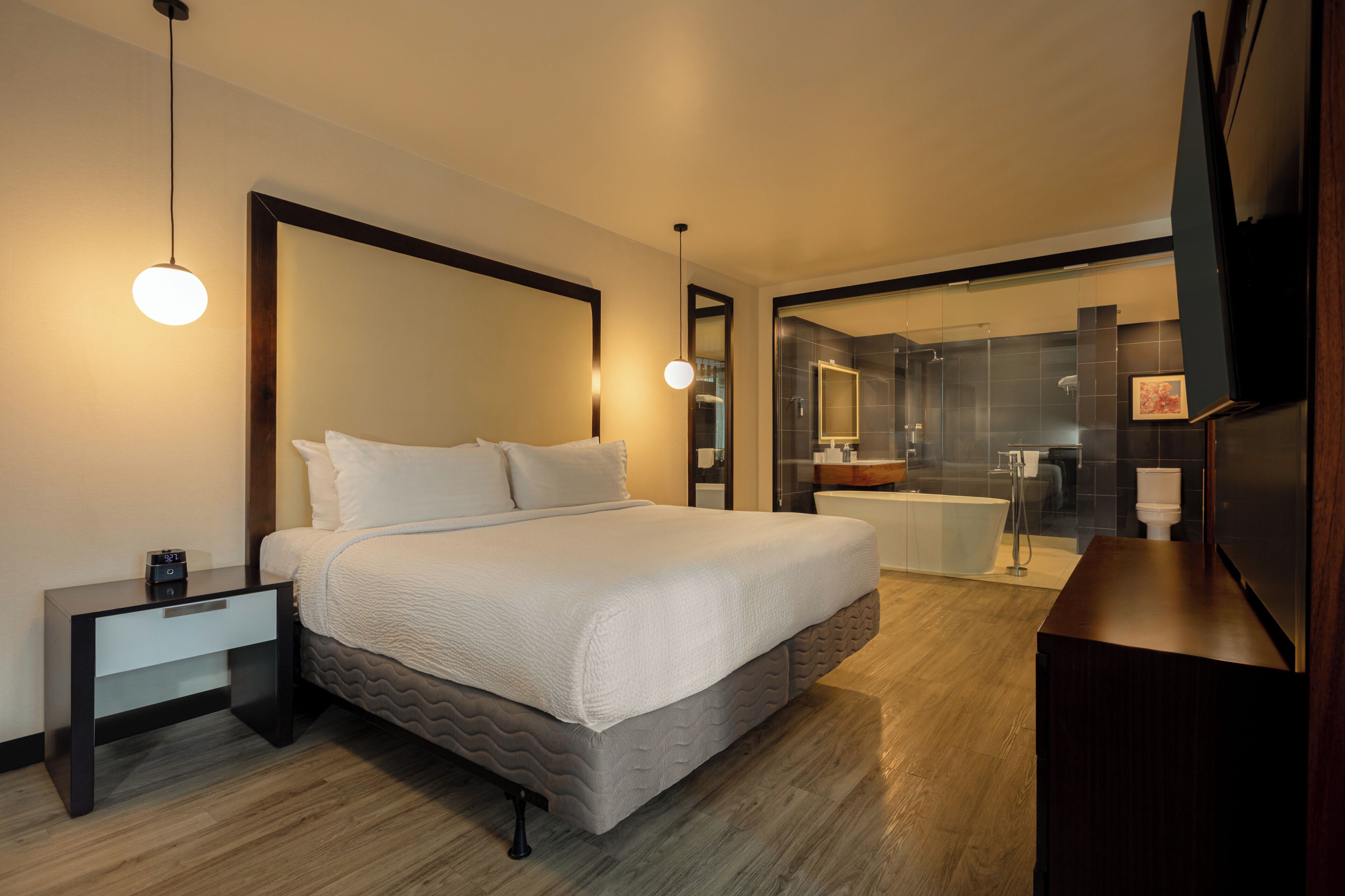 Una habitación de hotel moderna con una cama grande, mesita de noche y un baño con bañera y ducha.