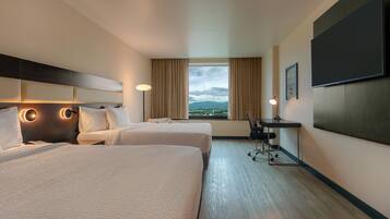 A hotel room with two beds, a desk, a chair, a TV, and a window with a view.