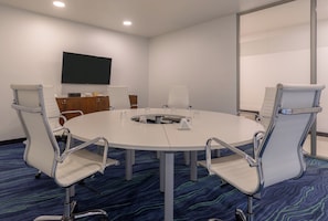 Une salle de conférence équipée d’une table ronde, de quatre chaises, d’un téléviseur à écran plat et d’une grande fenêtre.