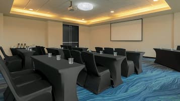A conference room with a projector screen, multiple tables with chairs, and a carpeted floor.