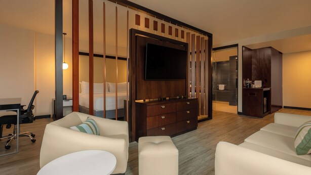 A modern hotel room with a flat-screen TV, a sofa, a dining table, a desk, and a wardrobe. - Four Points by Sheraton San Jose Sabana (San José)