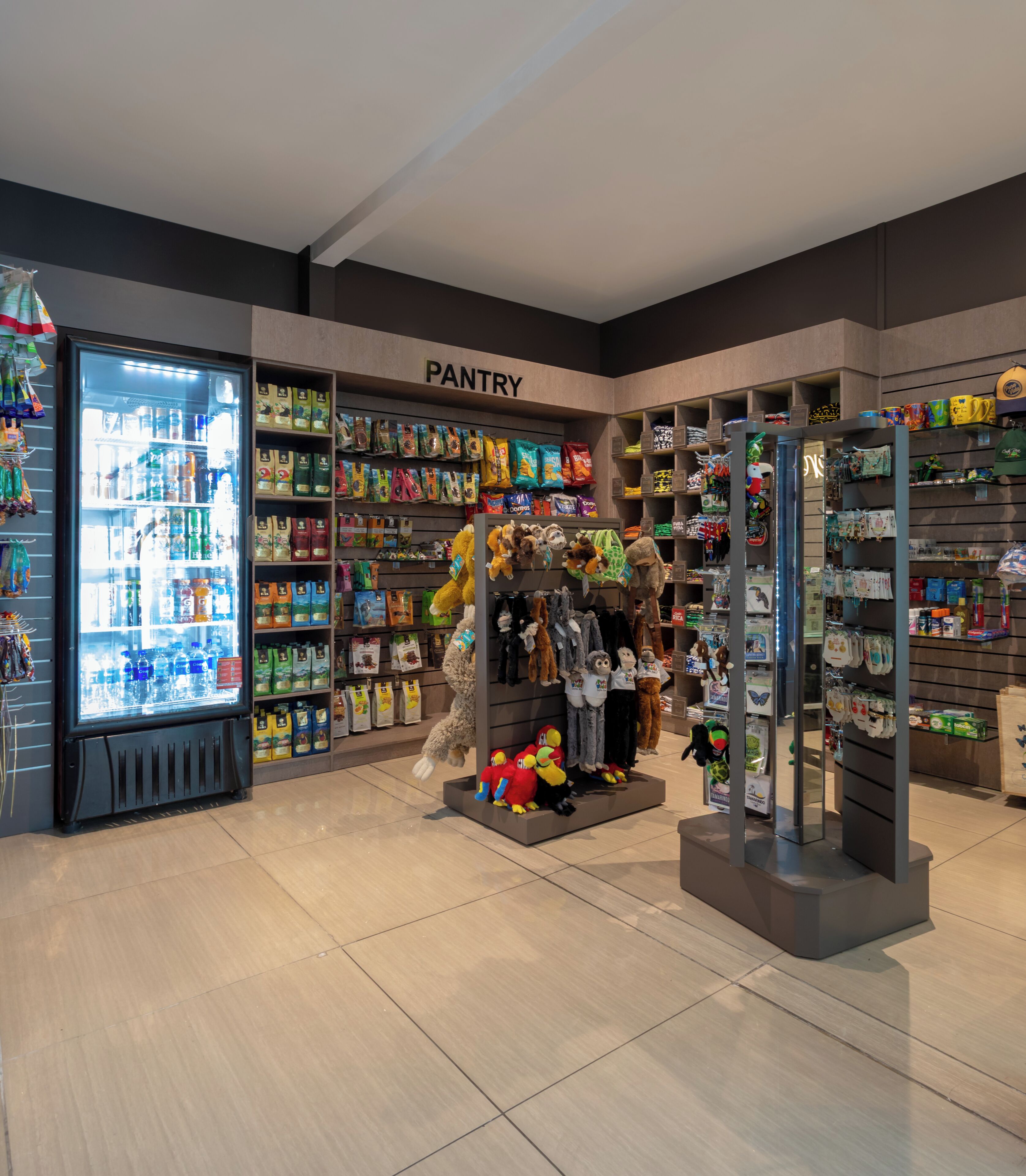 A store interior with a refrigerated section on the left, shelves stocked with snacks and groceries, and a display of plush toys in the center.